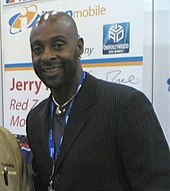 A bald Jerry Rice smiles. He is wearing a black suit.