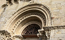 Photo de la voute romane d'un portail. Une corniche sculptée ceinture le mur dans le prolongement des chapiteaux du portail.