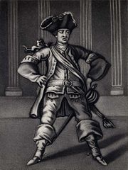 Acteur vu de face, jambes écartées, en tenue militaire, noir et blanc sur fond de colonnes de style dorique.
