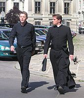 Priester met priesterhemd (priesterboordje verwijderd) en priester met soutane.