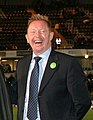 A laughing Caucasian man in a black suit with short blonde hair.