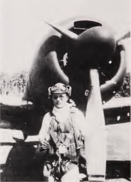 Photo noir et blanc d'un homme en tenue de pilote, devant l'hélice d'un avion.