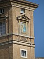 Farbfotografie vom oberen Teil eines Backsteingebäudes. Neben vier Fenstern, die sich auf drei Stockwerke verteilen, ist eine fenstergroße Malerei von Maria und Jesus mit einem dreieckigen Fenstergiebel. Unter der Malerei befindet sich ein blau-gelber Wappen und rechts davon die Aufschrift „Totus Tuus“. Unter dem Fenster mit der Malerei steht „Mater Ecclesiae“.