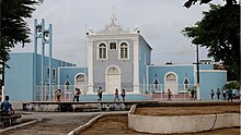 Imagem da Igreja Matriz de Santo Antônio de Pádua, com pessoas caminhando na calçada em frente à igreja, e partes da Praça Coronel Lucena Maranhão em primeiro plano.