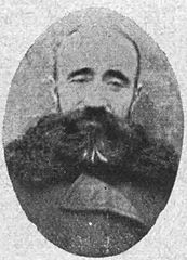 Fotografia czarno-biała, owalny portret białego mężczyzny w średnim wieku w płaszczu z zapewne futrzanym kołnierzem, mężczyzna ma głęboko osadzone oczy, ciemne wąsy i brodę oraz krótkie włosy