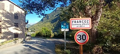 Photographie d'un panneau de Francoz, écrit en noir, où la limitation de vitesse est de 30 km/, devant des immeubles.