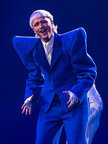 Photo of Joost Klein while performing, wearing a white sleeveless shirt and pink-shaded glasses