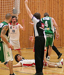 Un arbitre le bras levé, à côté d'un joueur au sol.