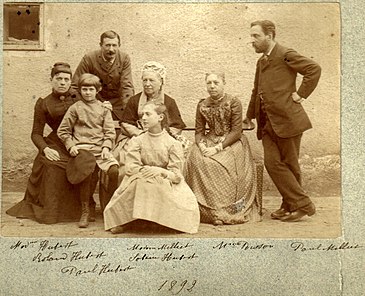 Photograph of the Miliet family outdoors. On the left, Louise Milliet, aged thirty-eight, is sitting on a bench with her two children in front of her. Her husband is standing behind her. On the right are Alix and Paul Milliet, aged fifty and forty-eight. Louise Milliet, aged seventy, sits in the middle of the bench and separates the siblings.