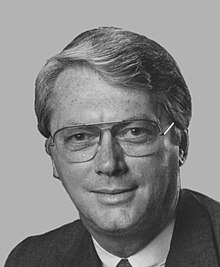 A color portrait of a gray-haired man in his seventies wearing a suit