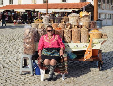 Продавачица сувог воћа и орашастих плодова на улици у португалском месту Назаре. Назаре је популарно одмаралиште на обали Атланског океана. Жена на слици носи одећу украшену традиционалним португласким везом