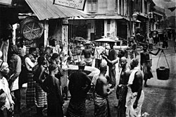 Men of various ethnicities - Chinese, Malay, and Indian gather at a street corner in Singapore, circa 1900. Photographic Views of Singapore Plate 23 Street Scene.jpg