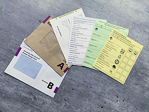 Two envelopes, a postal voting slip and three differently coloured ballot papers on a table