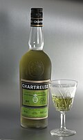 Une bouteille de Chartreuse verte, accompagnée d'un verre.