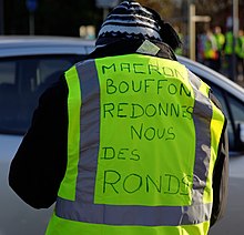 Manifestant de dos, habillé d'un gilet réfléchissant avec écrit : « Macron bouffon redonnes nous des ronds. »