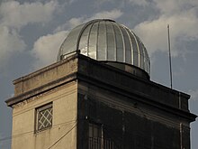 Foto de la parte superior de una torre y sobre ella una cúpula plateada de observatorio astronómico.