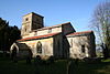 A stone church with red tiled roofs seen from the southeast, showing the chancel, the south aisle, clerestory and porch, and the tower plain parapet