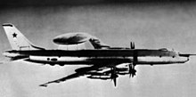 photo noir et blanc d'un avion-radar en vol. C'est un Tu-114 sur lequel a été montré un dome radar, en forme de soucoupe, au dessus de l'arrière du fuselage.