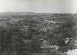 Photographie en noir et blanc représentant le viaduc en courbe surplombant une vallée boisée et cultivée.