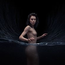 A nude Leanne Macomber stands with the bottom-half of her body in water.