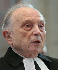 Three-quarter profile of elderly priest, with short, white hair brushed back, wearing clerical bands.