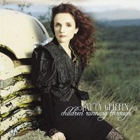 Patty Griffin sitting on the bumper of an old rusted truck in a field. Her hair blows in the wind.
