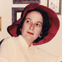 3/4 view of a tightly cropped headshot of a woman with a flowy red hat and a white shirt