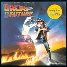 Michael J. Fox stepping out of a partially-visible DeLorean with lines of fire trailing behind, looking astonishingly at his wristwatch. A sticker on the upper right says "Featuring "The Power of Love" by Huey Lewis and the News".
