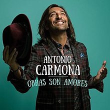 A color image of a man with his head looking up and smiling, and holding a hat in his left hand. The words ANTONIO CARMONA are written in white capital letters at the middle, while OBRAS SON AMORES is written in light green capital letters in the lower part of the image.