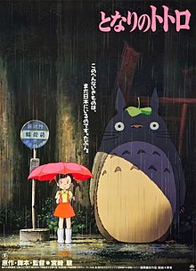 An early version of Satsuki is near a bus stop on a rainy day holding her umbrella. Standing next to her is Totoro. Text above them reveals the film's title and below them is the film's credits.