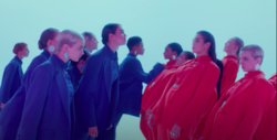 Dua Lipa and her crew of women wearing blue suits lean over toward their clones, wearing red, in a blue-tinted room.