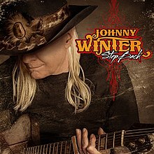 Johnny Winter, eluzante larĝrandan ĉapelon kaj ludantan gitaron