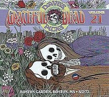 Two skeletons, a man and a woman, lying together in the grass and flowers, with the Boston skyline in the background