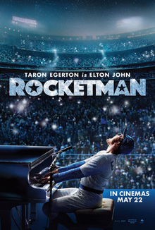 Taron Egerton (portraying as Elton John, seen wearing a Los Angeles Dodgers baseball uniform) plays the piano in front of concert goers at a stadium. On the film's title, stars are placed in the letters "O" and "A".