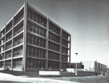 Screenshot of a digitized ROMA brochure. Image shows the Theoretical and Computation Building for the Atomic Energy Commission. The building is modern in design, with delineated segments splitting the building's facade in rectangles both vertical and horizontal. The photograph is in black and white.
