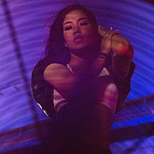 An image of Jhené Aiko posing in blue/purple lighting