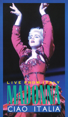 Madonna in short cropped hair, wearing a red flamenco dress. She puts up both of her hands above her head