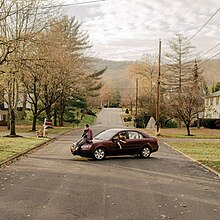 A photograph of youth lounging on a car on a desolate road