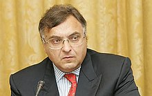 Headshot of a suited man sitting behind a microphone