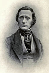 фотография человека, смотрящего на зрителя, но смотрящего вниз, одетого в викторианском стиле с широким шелковым галстуком и булавкой для галстука