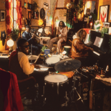 Individual men playing the drums, piano, guitar, trumpet and saxophone in a small and cramped room