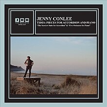 A photo of Conlee with an accordion, standing on a small platform on the shore