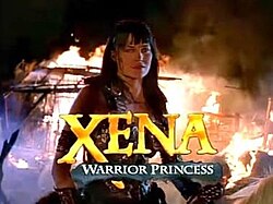 A woman in leather armor sits on horse back with flames behind her. At the bottom of the screen in capital letters is the word "Xena" in gold lettering.