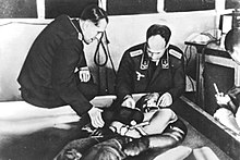 A cold water immersion experiment at Dachau concentration camp presided over by Ernst Holzlohner (left) and Sigmund Rascher (right). The subject is wearing an experimental Luftwaffe garment. Dachau cold water immersion.jpg