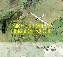 An aerial photograph of green fields with a white model aircraft flying above. In the centre there is large yellow text with the words "Mike Oldfield" and "Hergest Ridge". The lower portion of the image has a grey overlay with the words "Deluxe Edition" at the lower right.