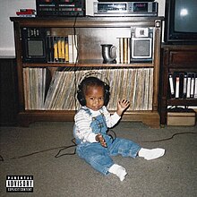 A photo of a Black baby sat on the floor of a living room, wearing headphones which are plugged into a record player.
