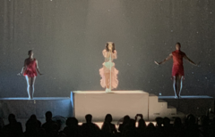 A color photograph of Marina performing live with backup singers while flowing their arms.