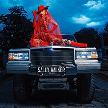 Azalea posing on the hood of a monster-truck hearse wearing a giant red veil.