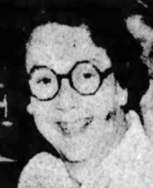 A smiling white woman with dark hair and octagonal eyeglasses
