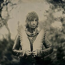 Arthur in a black-and-white photo, cradling a sculpture of wings